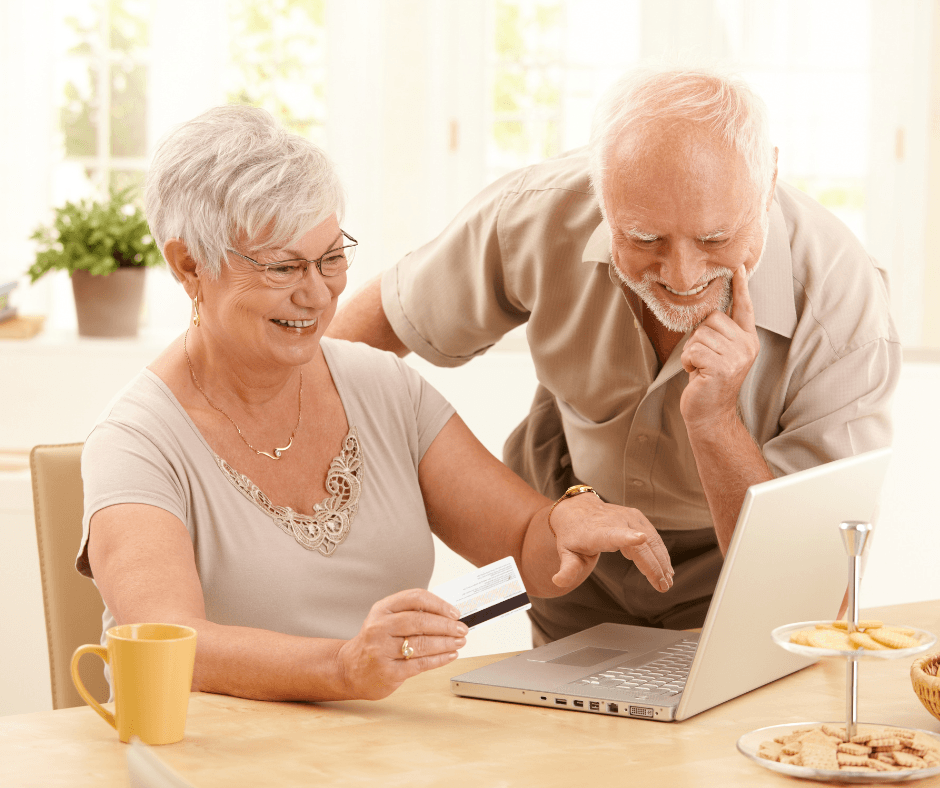 A man and a woman are sitting at a table looking at a laptop computer.