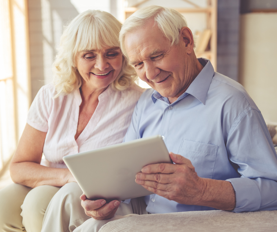 A man and a woman are sitting on a couch looking at a tablet.