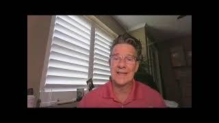 A man wearing glasses and a pink shirt is sitting in front of a window.