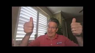 A man in a red shirt is giving two thumbs up in front of a window.