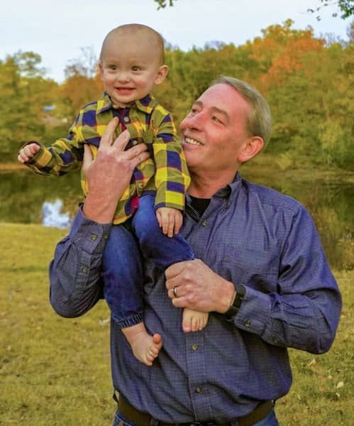 A man is holding a baby on his shoulders in a field.