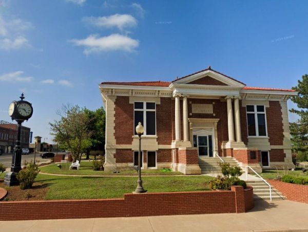 Ark City Kansas downtown mural Red brick Carnige library building in Perry, OK with white columns, clock on left, blue sky.
