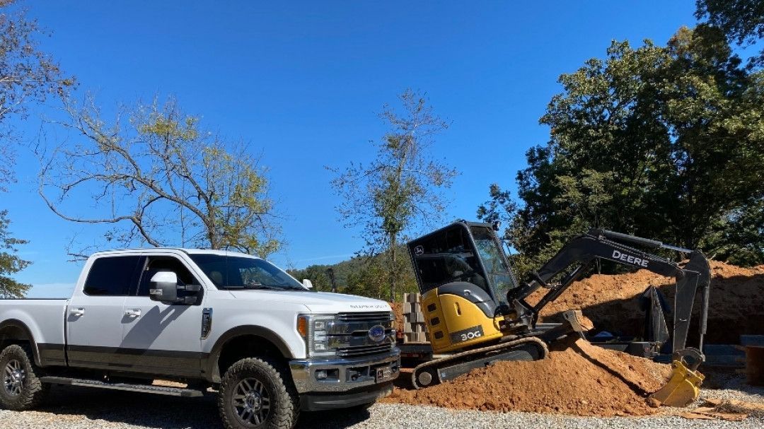 A white truck is parked next to a yellow excavator