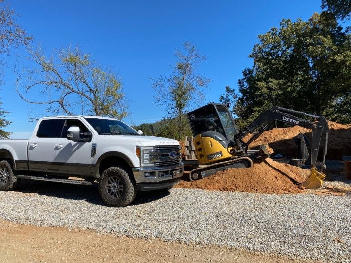 A white truck is parked next to a yellow excavator