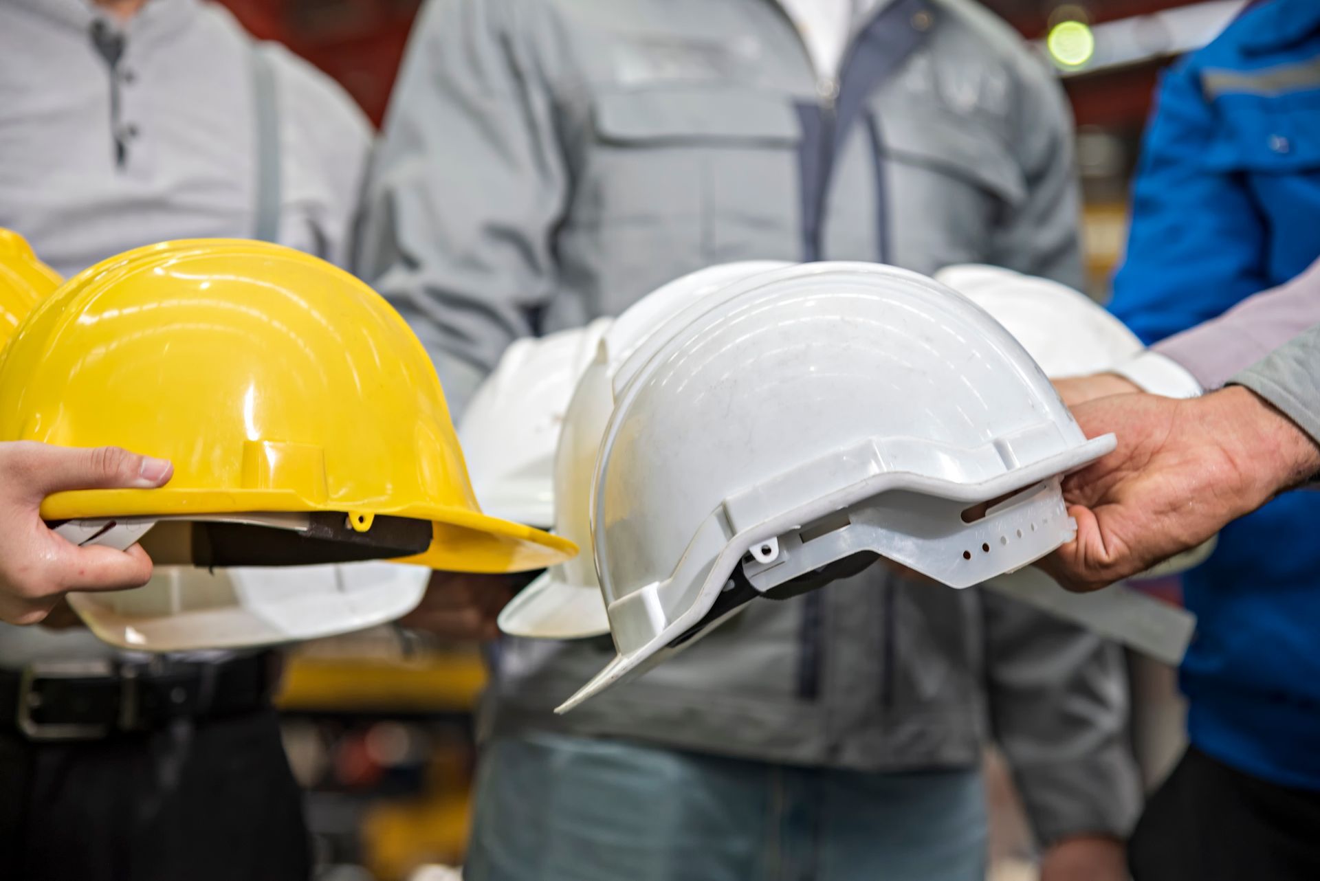 People holding yellow and white hard hats in a workplace setting.