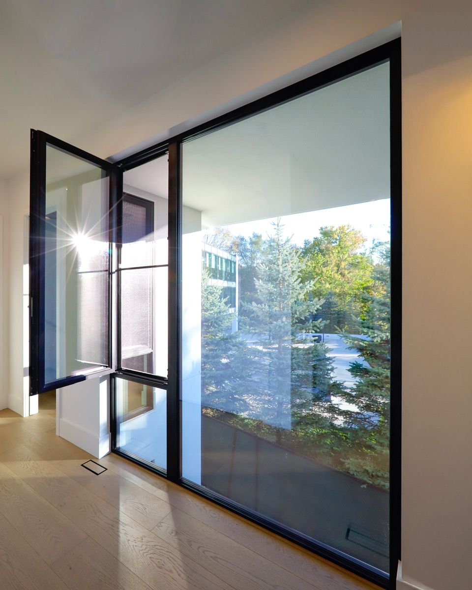 Large black-framed windows, one open, revealing a bright outdoor view and interior with wood floor.