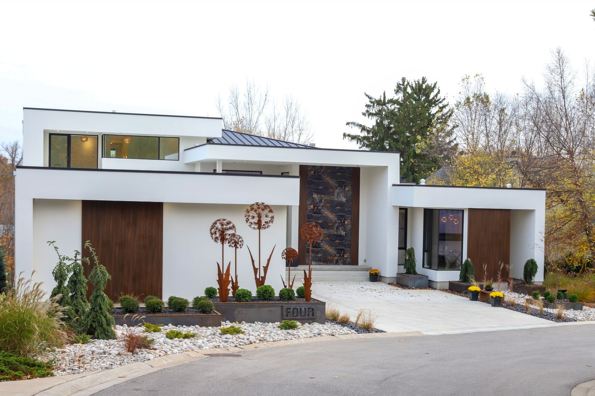 Modern white house with dark wood accents, concrete driveway, and landscaping.