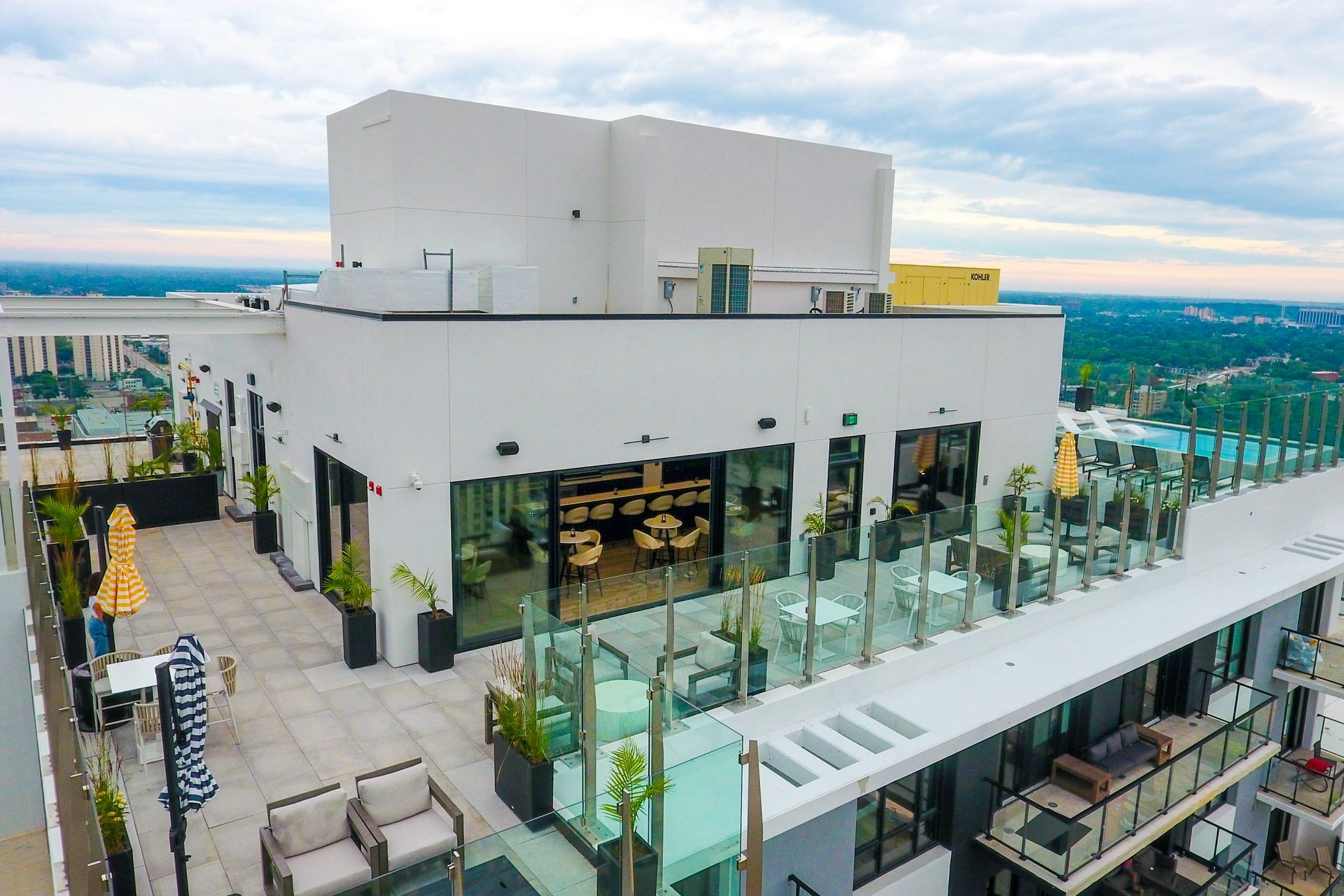 Rooftop restaurant with outdoor seating, glass railings, and city views. White building with open dining area.