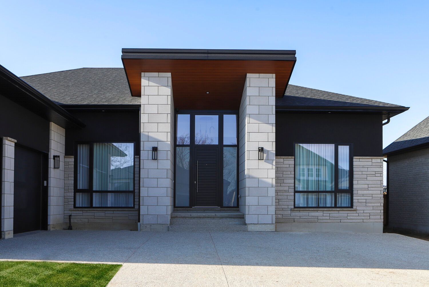 The front of a modern house with a black door and windows.