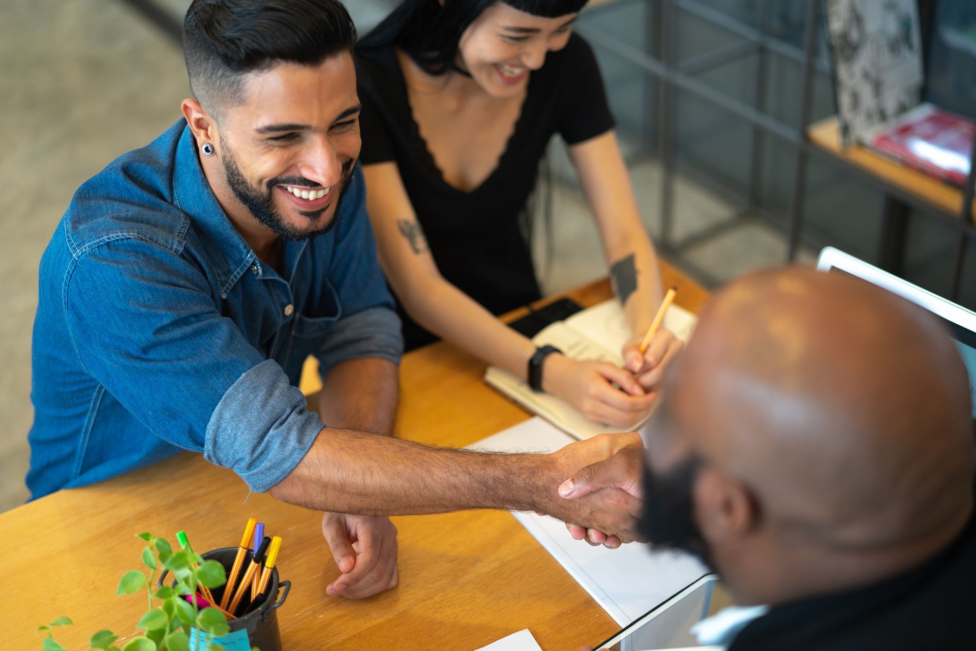 A man and a woman are shaking hands with a man at a table.