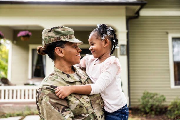 A military woman embraces her daughter in front of their house.