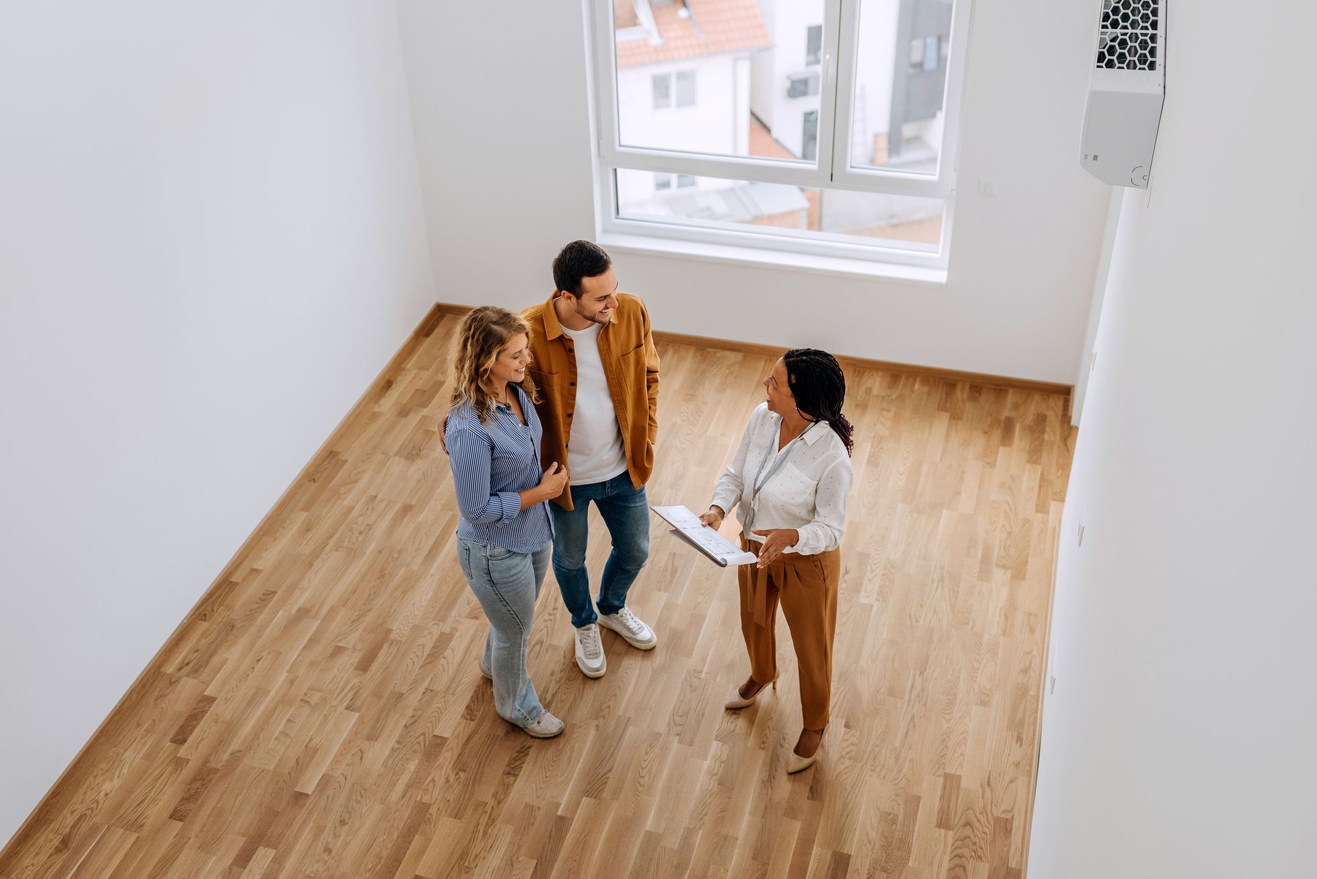 A man and a woman are standing in an empty room talking to a real estate agent.