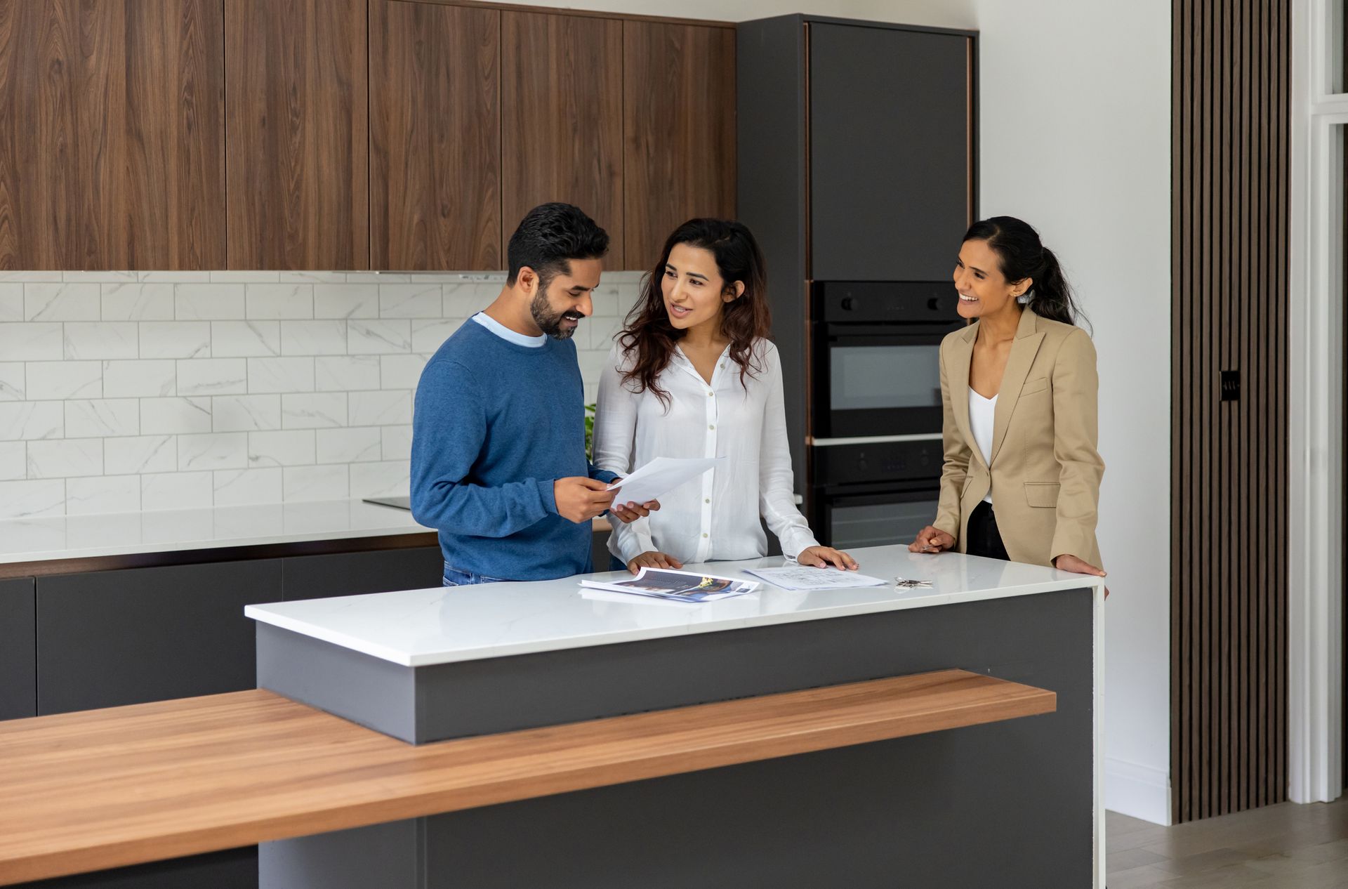 A man and a woman are standing in a kitchen with a real estate agent.