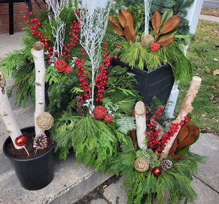A decorative red metal sleigh planter filled with green foliage and small red berries on an outdoor table.