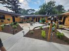 An outdoor courtyard with a central concrete patio, landscaped garden beds with brown mulch, and tan building exteriors.