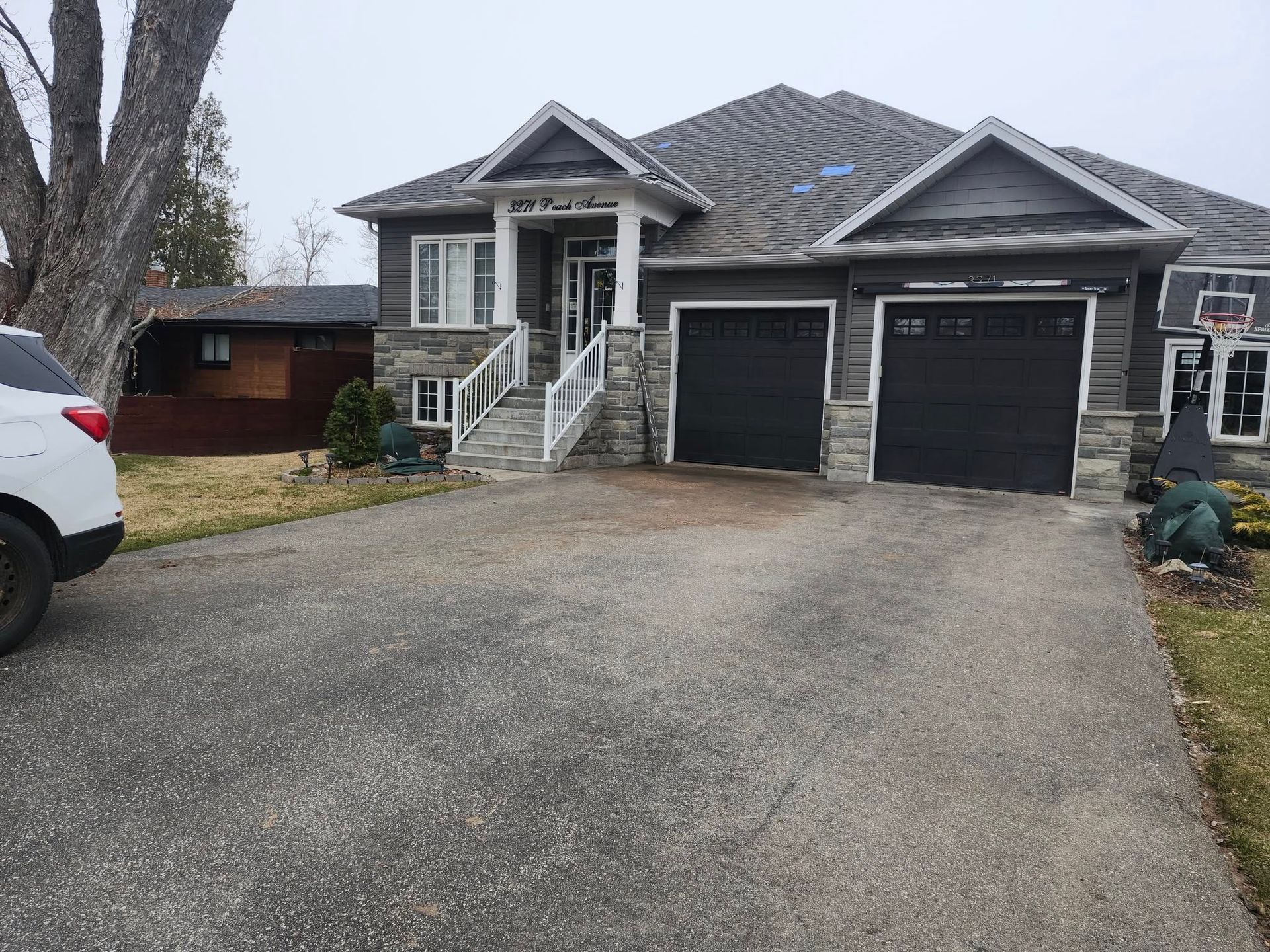 A gray two-story house with a double garage, stone accents, and a paved driveway, seen on an overcast day.
