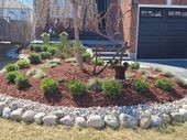 A garden bed with dark grey stone retaining walls, surrounded by green lawn, filled with shrubs and dark mulch.