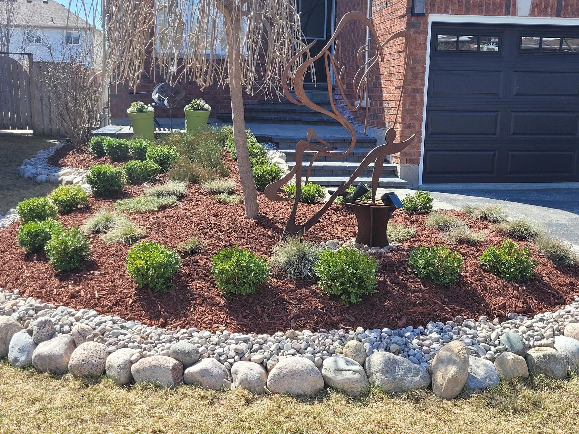 A garden bed with dark grey stone retaining walls, surrounded by green lawn, filled with shrubs and dark mulch.