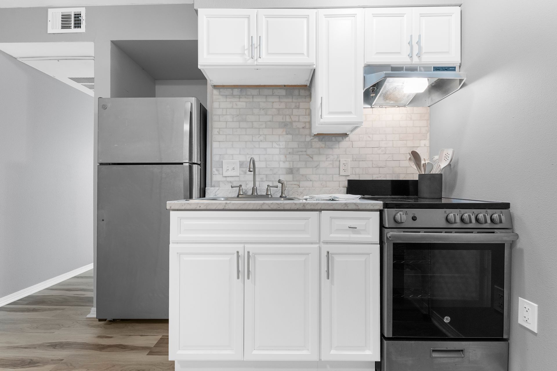 A kitchen with white cabinets , a stove , a refrigerator , and a sink.