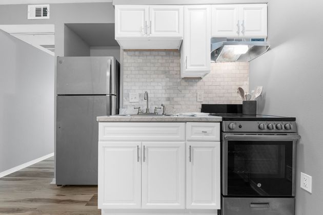 A kitchen with white cabinets , a stove , a refrigerator , and a sink.