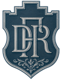 Escudo con monograma azul, letras plateadas ornamentadas y adornos decorativos sobre un emblema en forma de escudo.