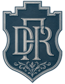 Escudo con monograma azul, letras plateadas ornamentadas y adornos decorativos sobre un emblema en forma de escudo.