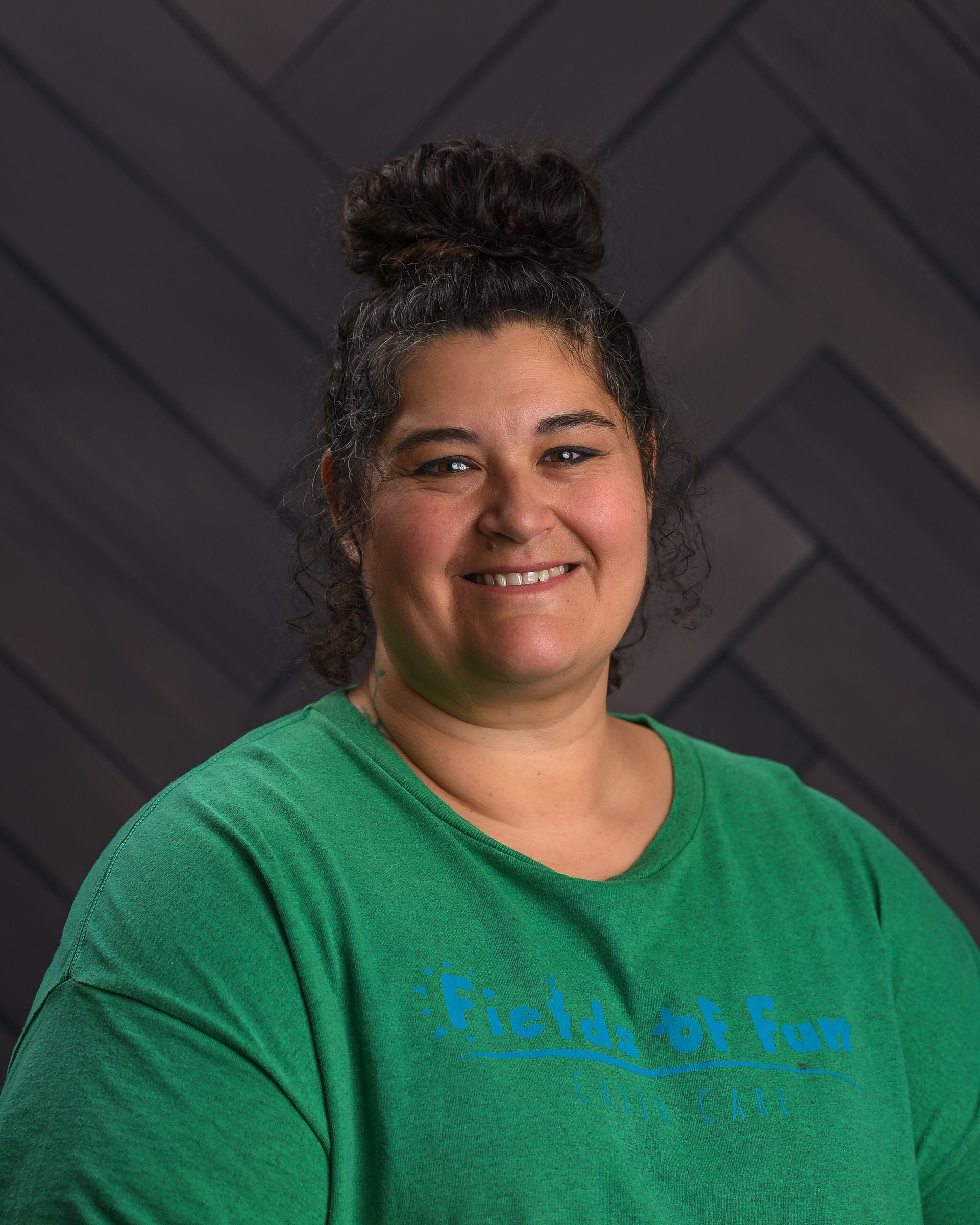 A woman wearing a fields of fun shirt is smiling for the camera.