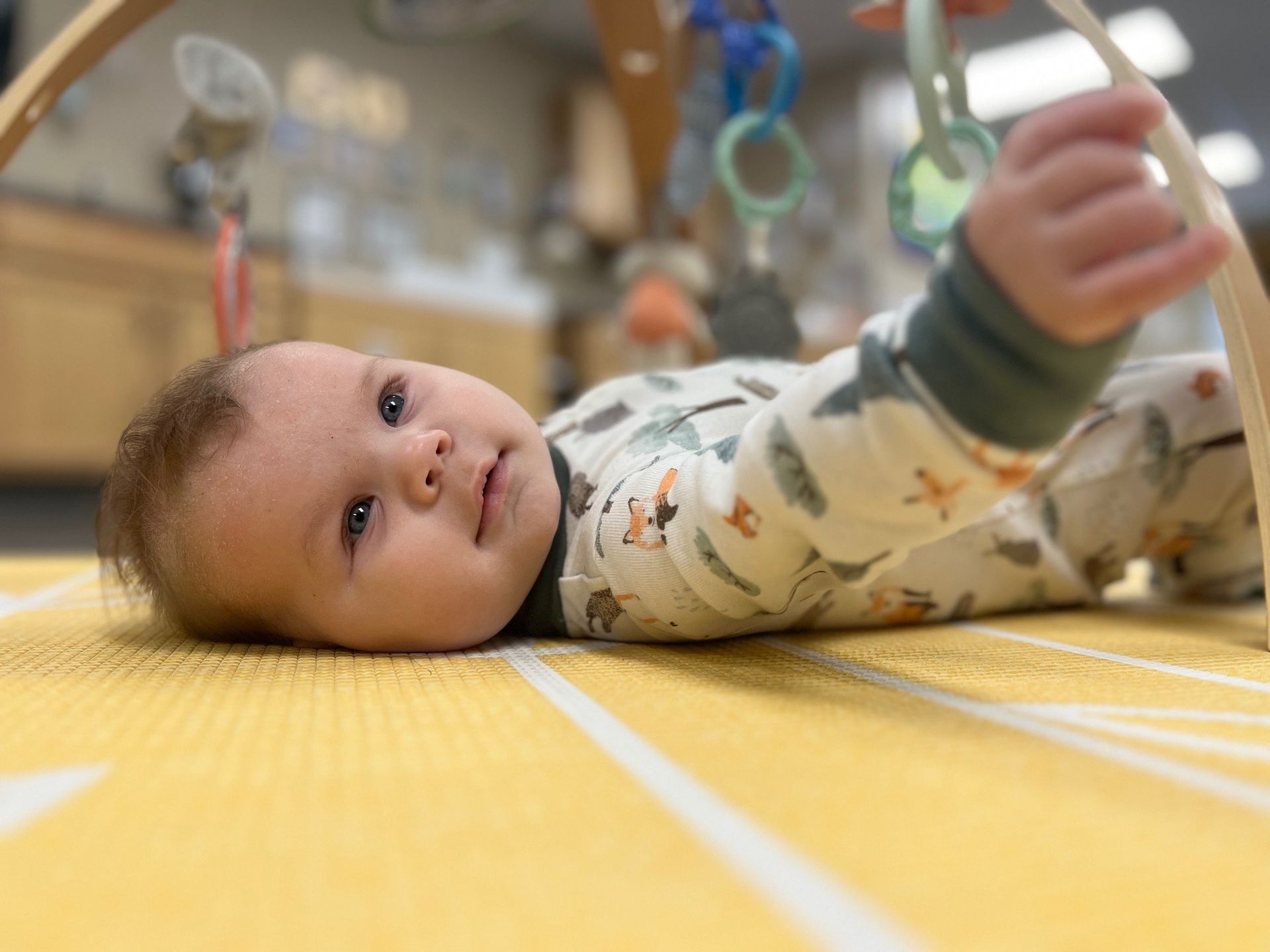A baby is laying on its stomach on a yellow mat playing with a toy.