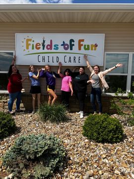 A group of people standing in front of a sign that says fields of fun child care.