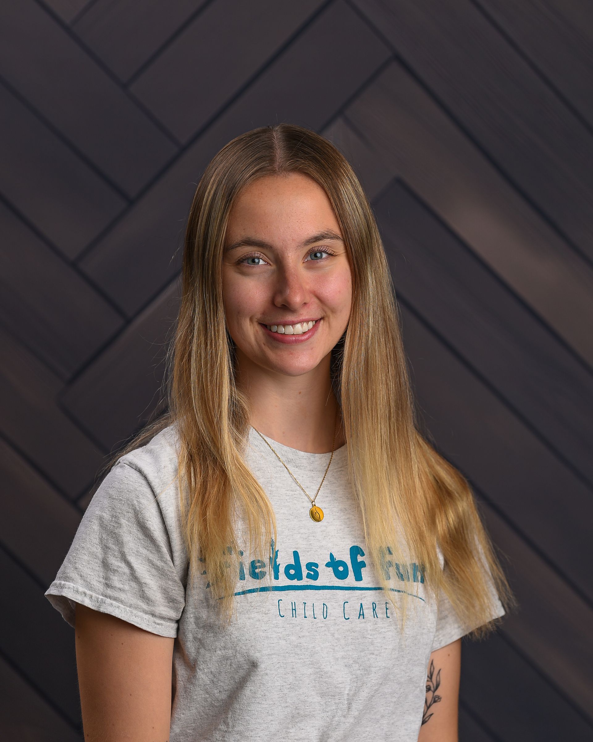 A young woman wearing a gray sweatshirt is smiling in front of a striped wall.