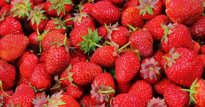A pile of strawberries with green stems on a table.