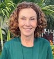 A woman with curly hair is wearing a green shirt and smiling for the camera.