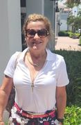 A woman wearing sunglasses and a white shirt is standing in front of a building.