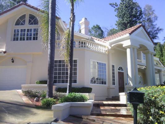 Large white house with columns, arched windows, and a front driveway on a sunny day