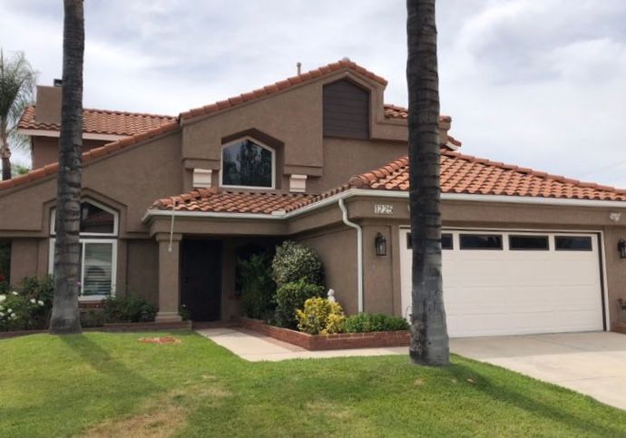 Two-story tan house with red tile roof, white garage, and palm trees in front yard