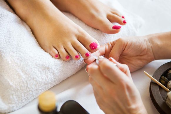 Manos pintando las uñas de los pies de rosa durante una pedicura sobre una toalla blanca.