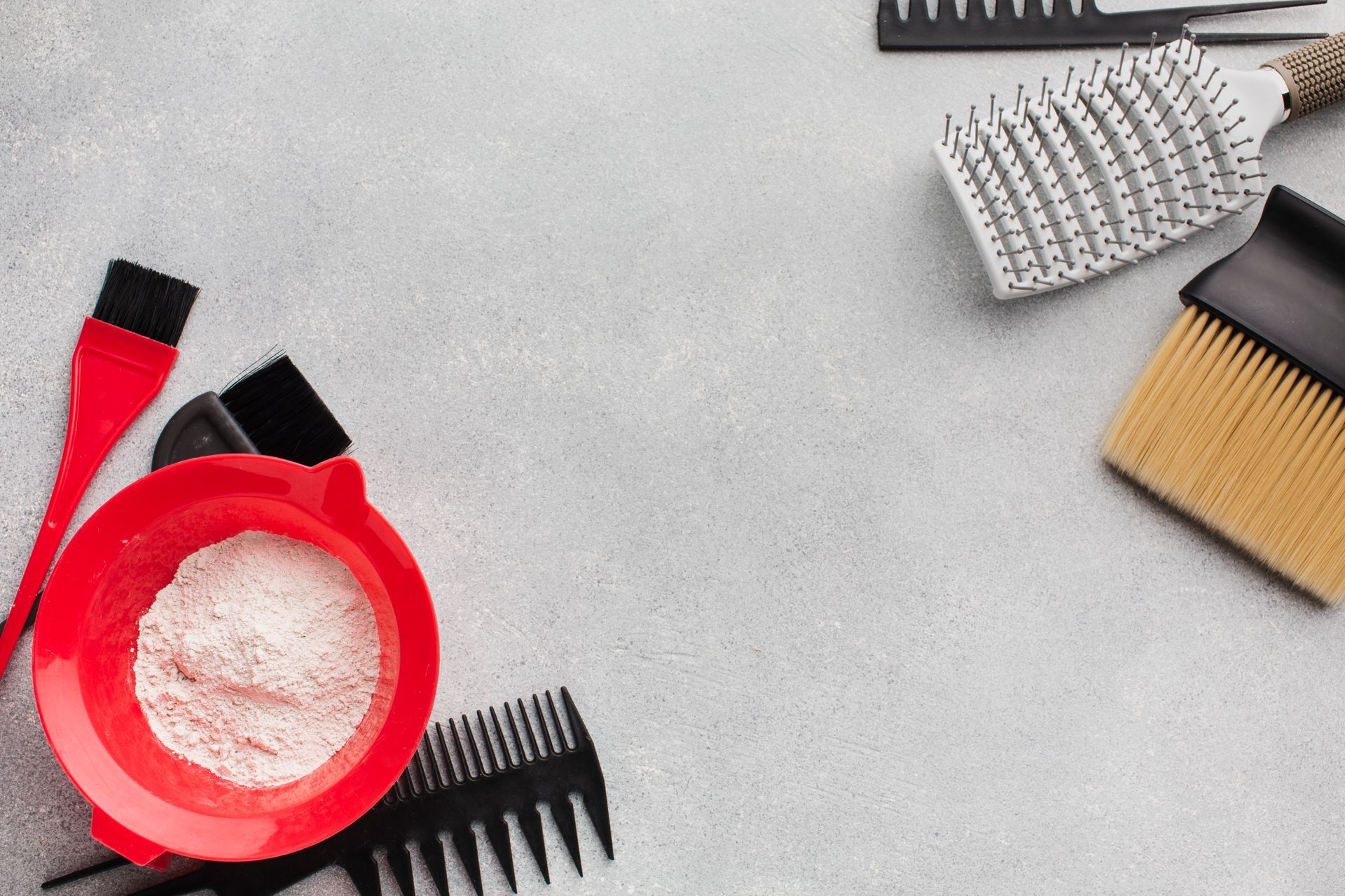 Bol para teñir el cabello con cepillos y peines sobre una superficie gris.