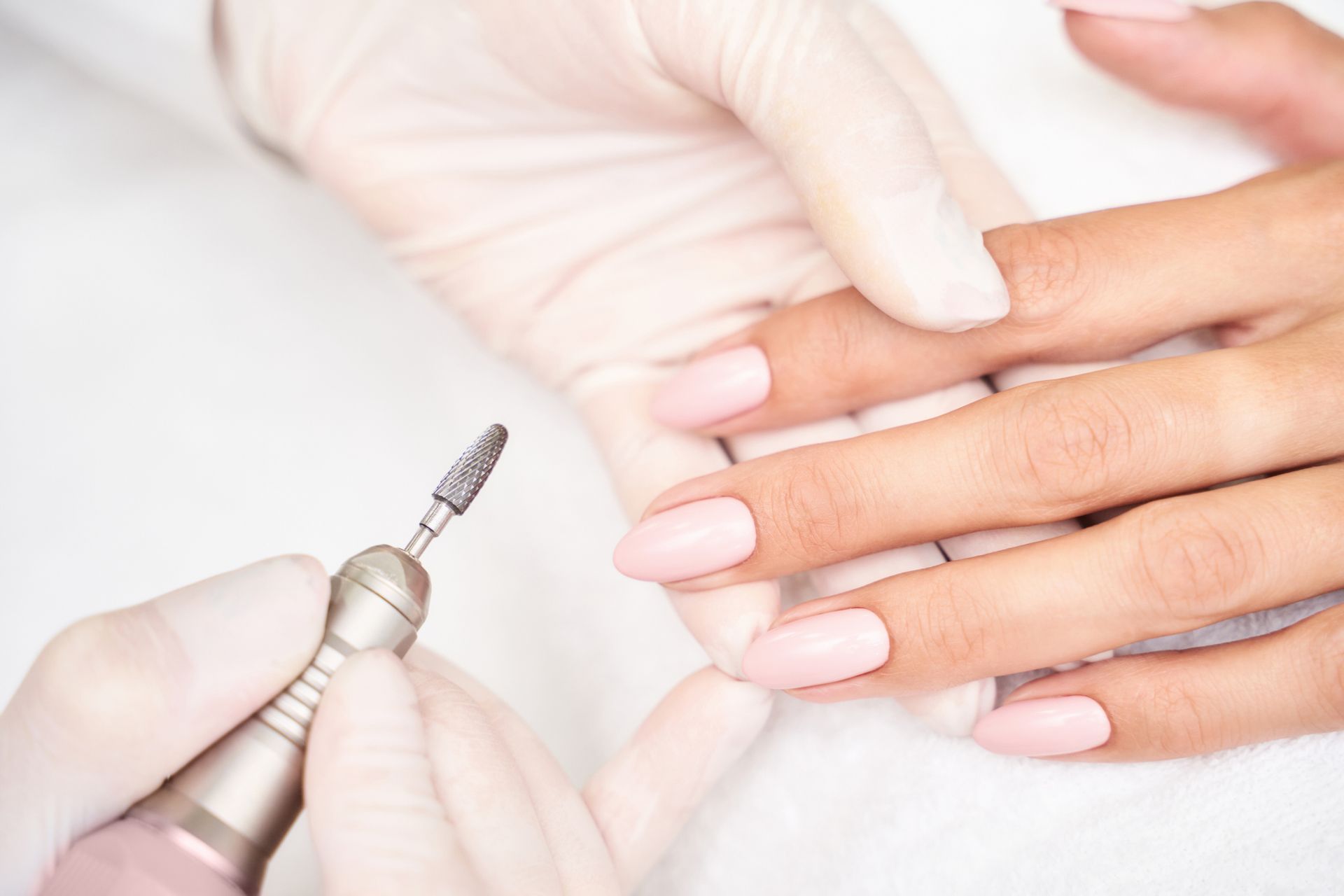 Uñas manicuradas siendo pulidas con un taladro de uñas por un técnico enguantado.