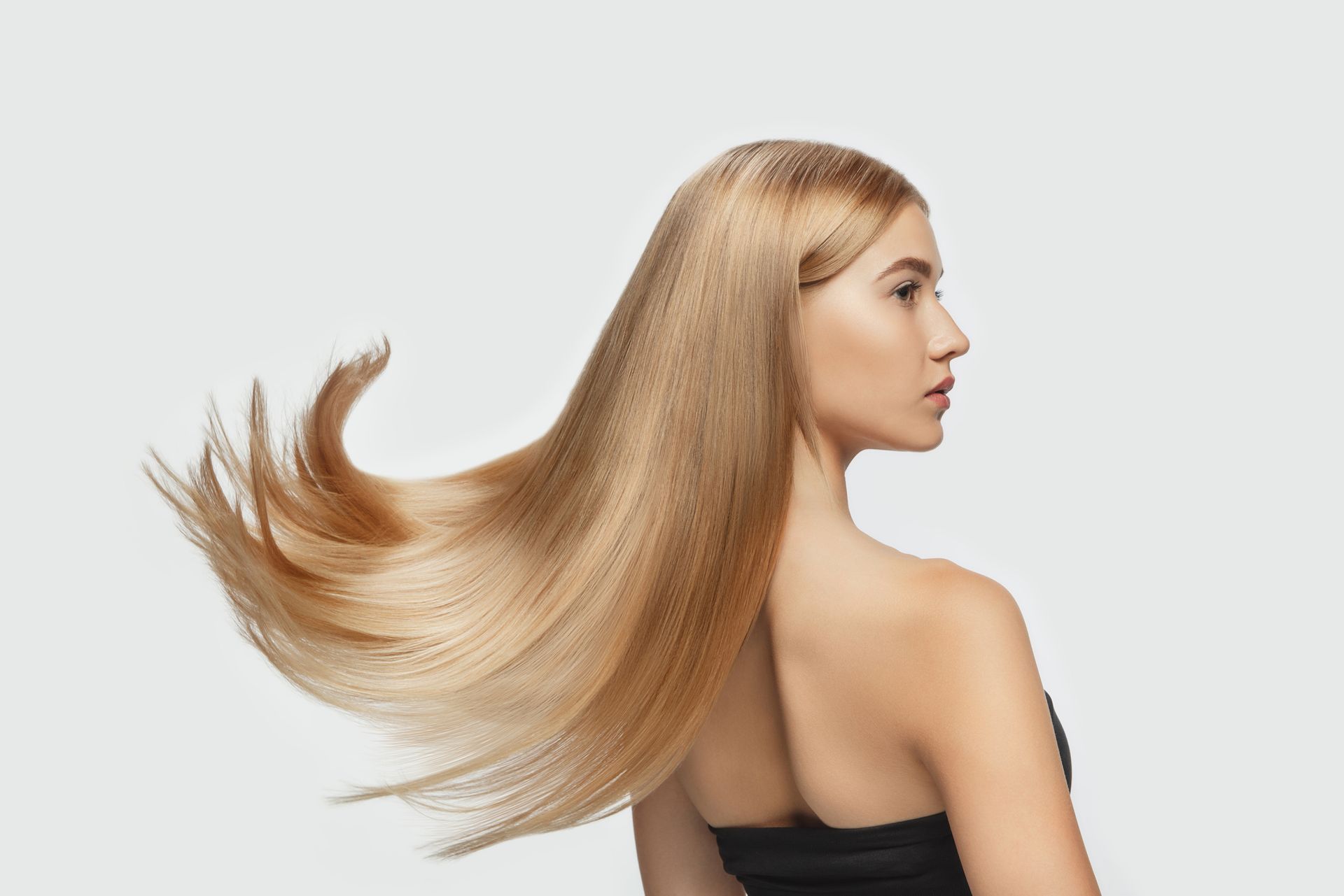 Mujer con cabello rubio largo que cae hacia atrás sobre un fondo gris claro.
