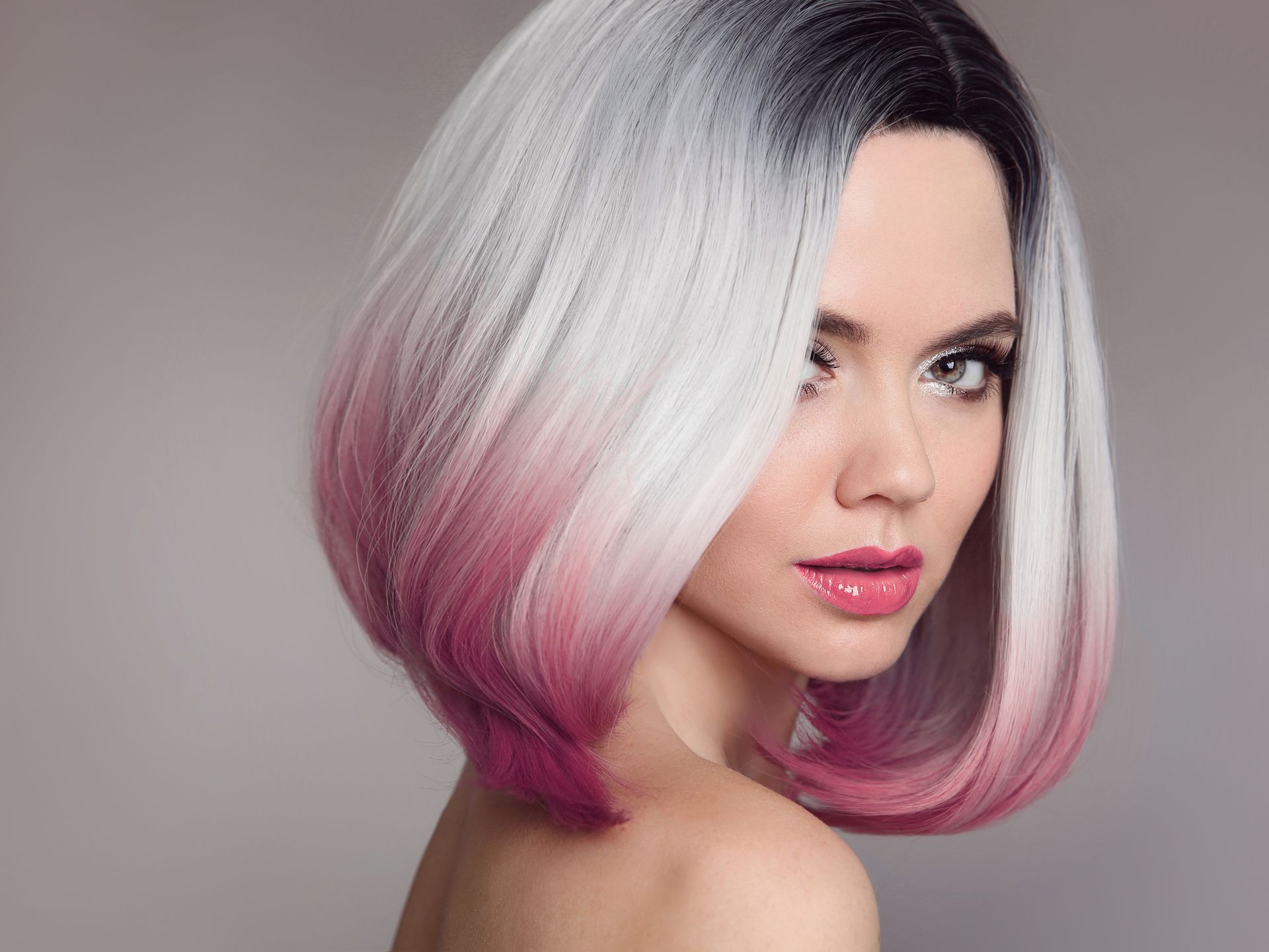 Corte de pelo bob plateado con puntas ombré rosas en una mujer sobre un fondo gris.