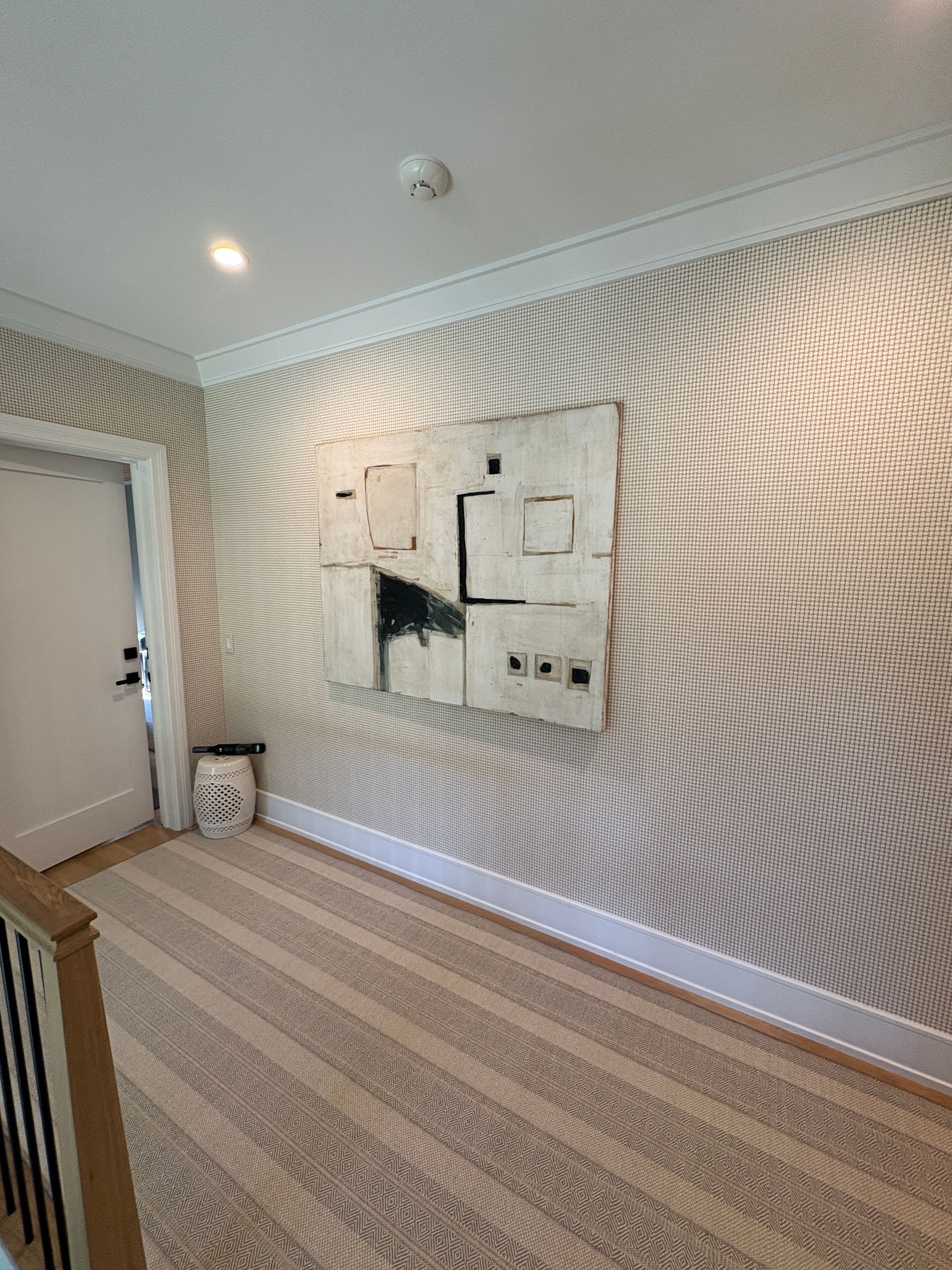 Empty hallway with patterned wallpaper, striped carpet, wall-mounted electrical panels, and a small trash bin.