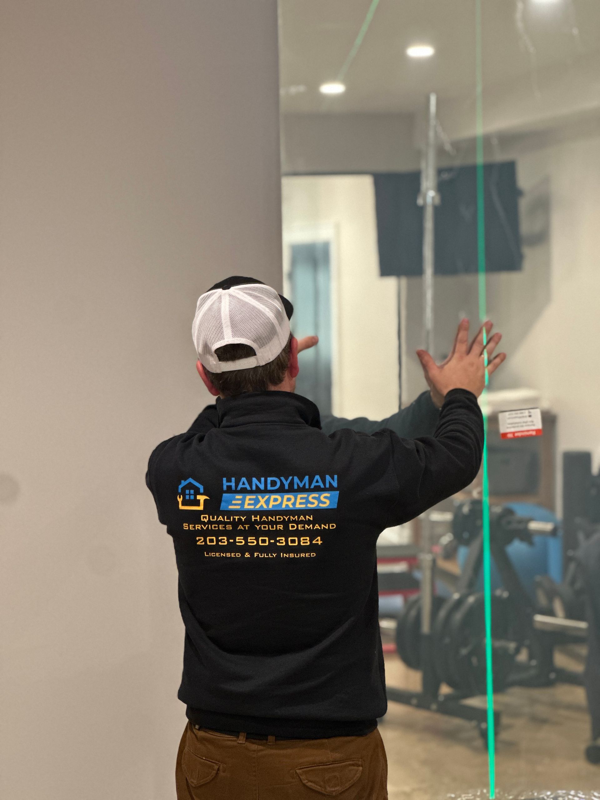 Handyman in black shirt and white cap gesturing at a glass wall inside a modern office