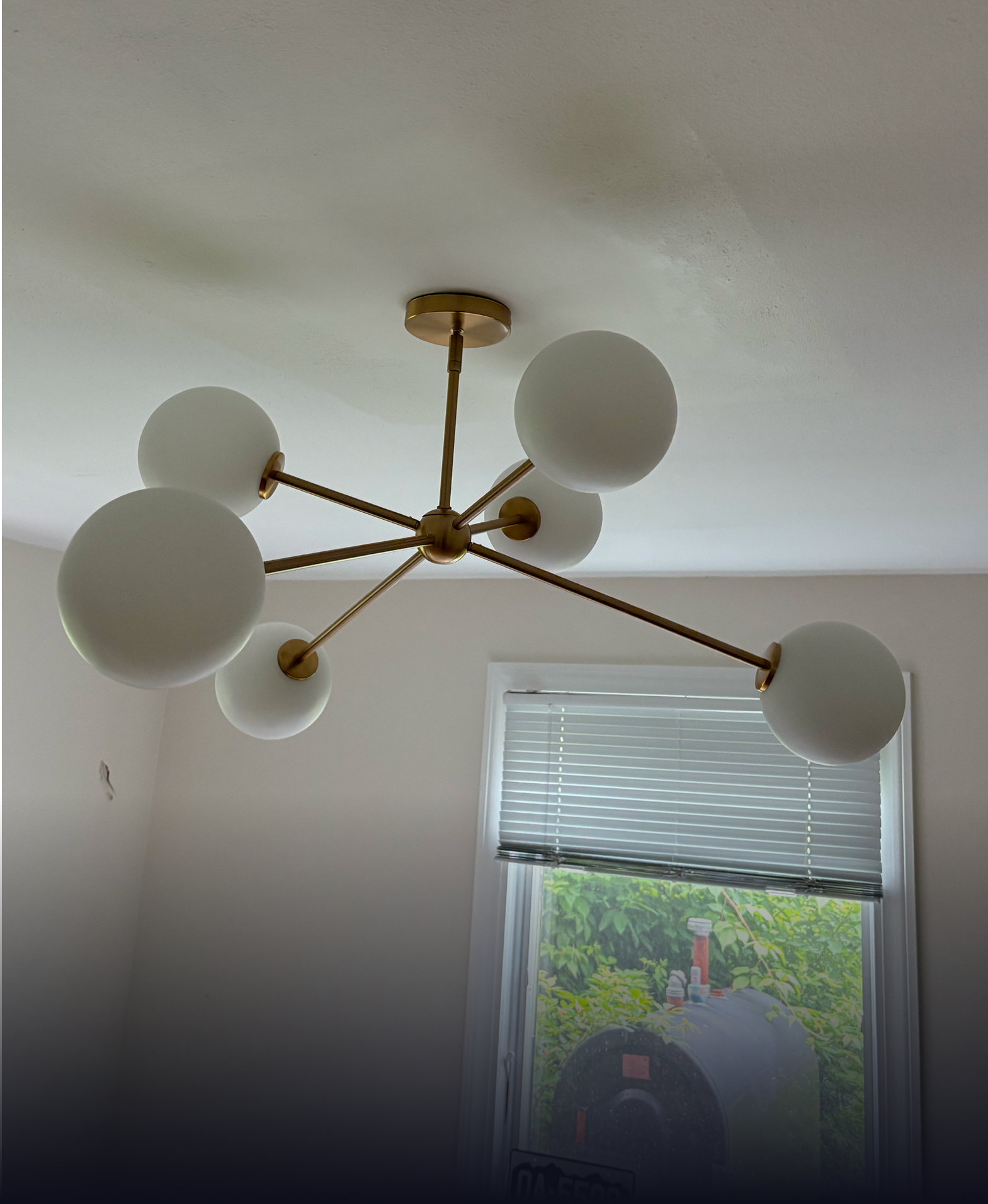 A brass mid-century modern chandelier with five white spherical glass shades mounted on a ceiling.