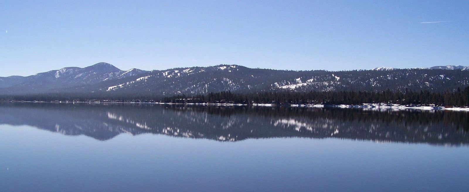 A serene lake reflects snow-dusted mountains under a clear blue sky.