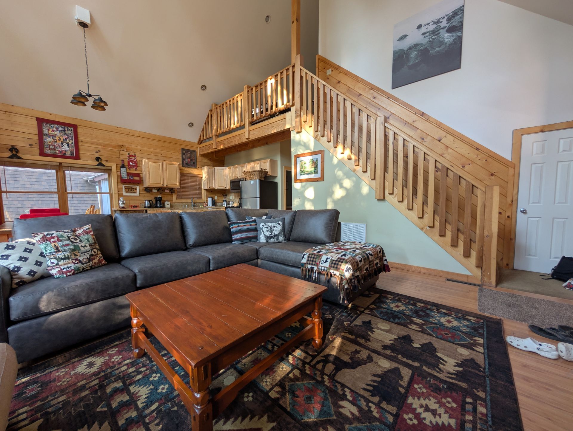 Cozy living room with a dark gray sectional, wooden staircase, and cabin-style decor.