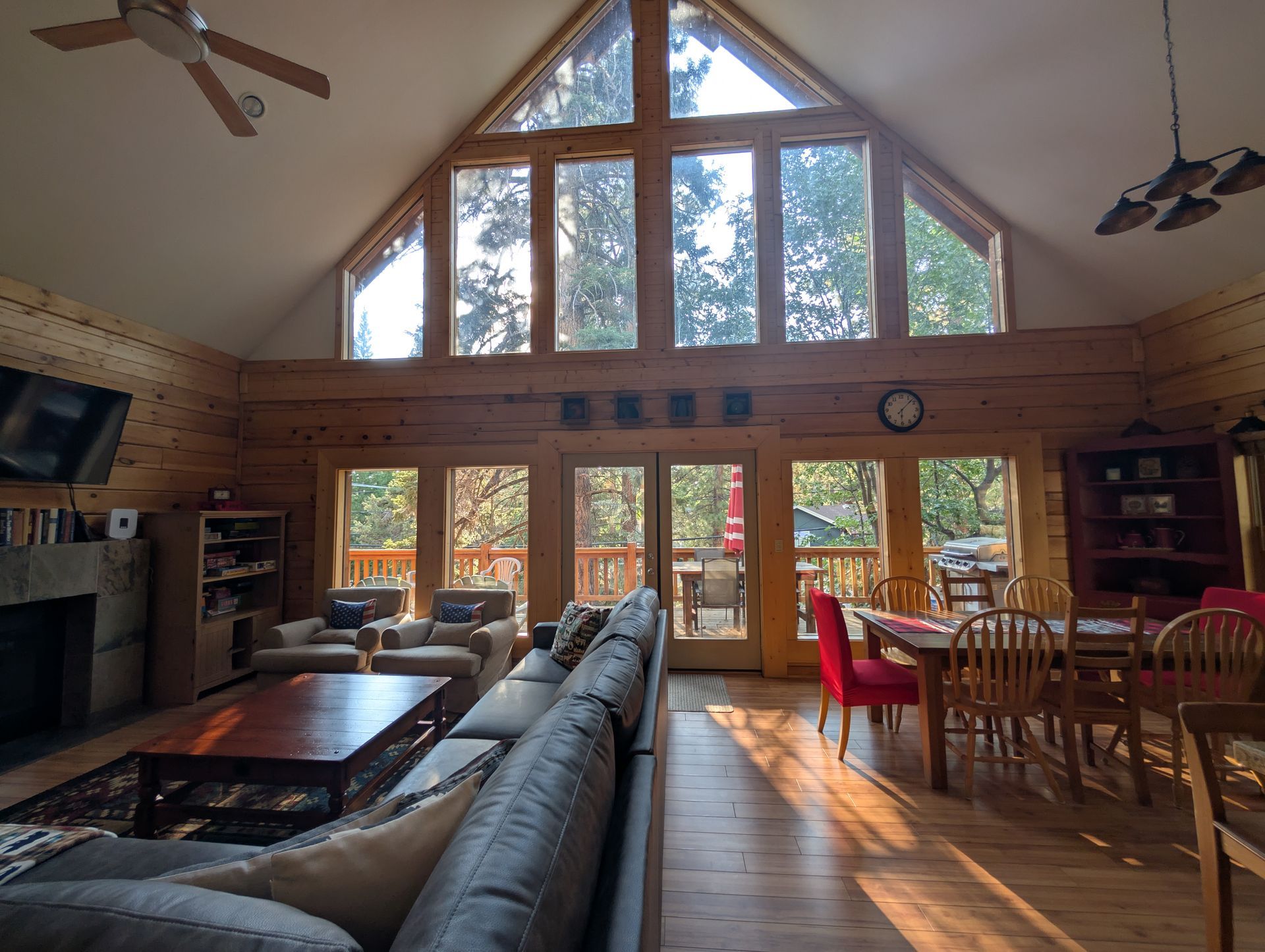 Three people sit on a large sofa in a wood-paneled room, with mountains visible through a large window.