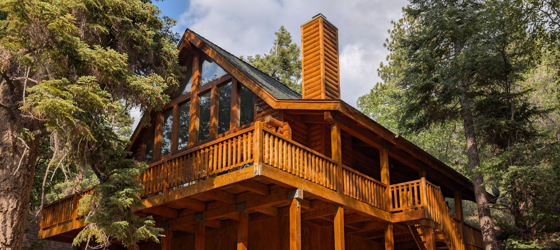 Wooden cabin with a deck, table, and chairs overlooking trees.
