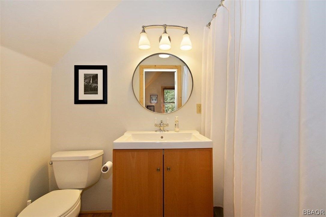 Bathroom with toilet, vanity, round mirror, and framed art; neutral colors.