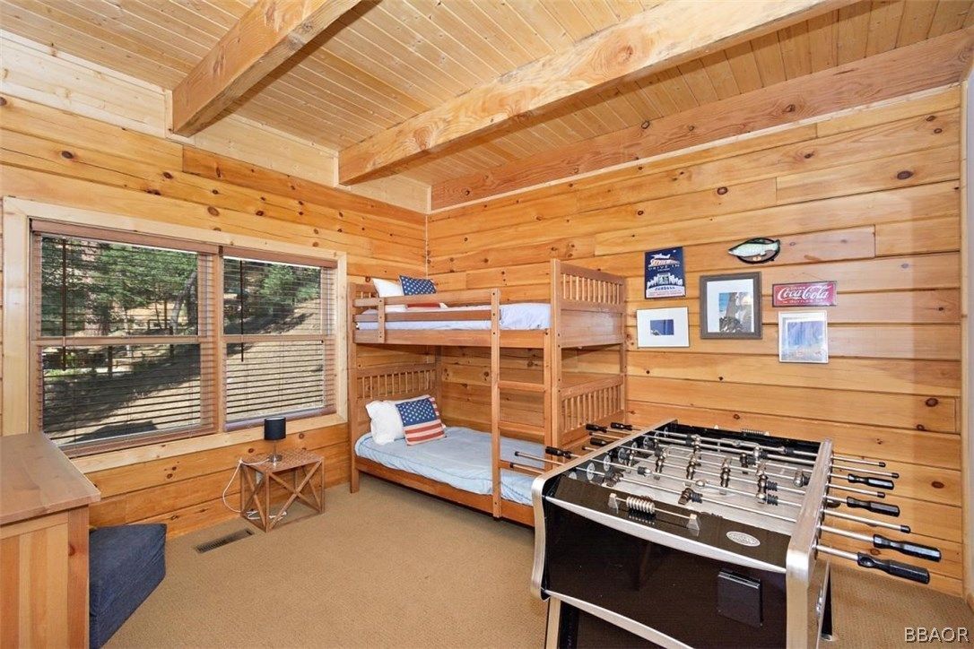 Log cabin bedroom with bunk beds, foosball table, and a window overlooking trees.
