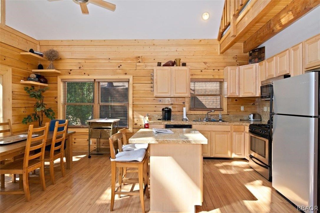 Wooden cabin kitchen with island, dining table, and stainless steel appliances. Light wood tones throughout.